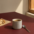 Dansk keramik kop i stentøj, håndlavet med blå streger står på et rødt bord med morgenmad 