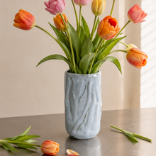 Håndlavet keramik vase lyseblå med tulipaner på et rustfrit stålbord. 