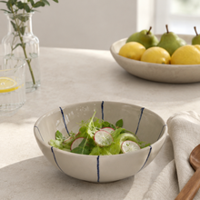 Stribet mellem keramikskål på et bord med salat og frugt