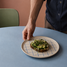 stor Stentøj tallerken holdes af en mand. Håndlavet tallerken med tern på et blåt bord med grøn stol.