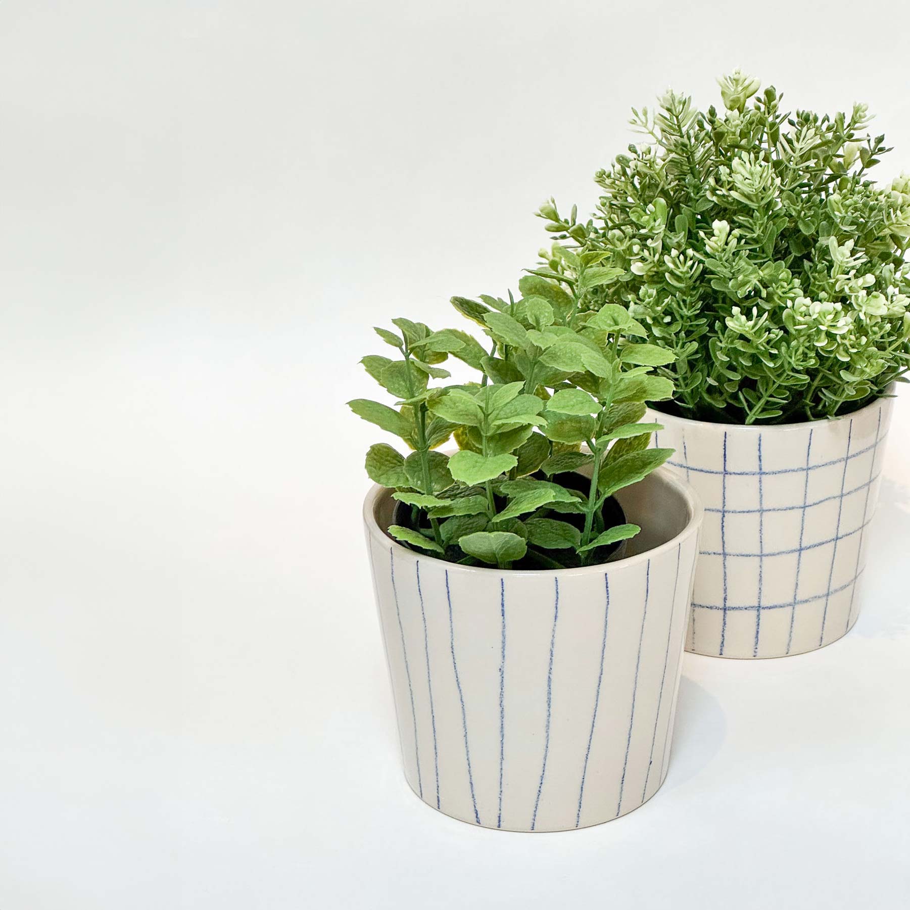 Håndlavede keramik urtepotter med blå striber og tern samt blank glasur, med grønne planter.