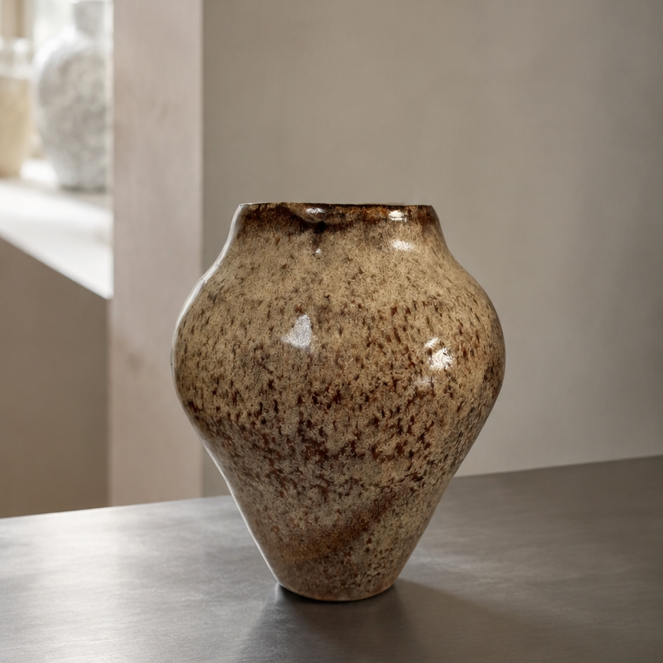Brun keramikvase med beige glasur står på et stålkøkken. 