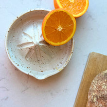 Citruspresser i keramik med appelsiner på lys bordplade.