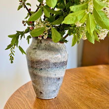 Keramik vase til blomster med grønne grene og hvide blomster på træbord.