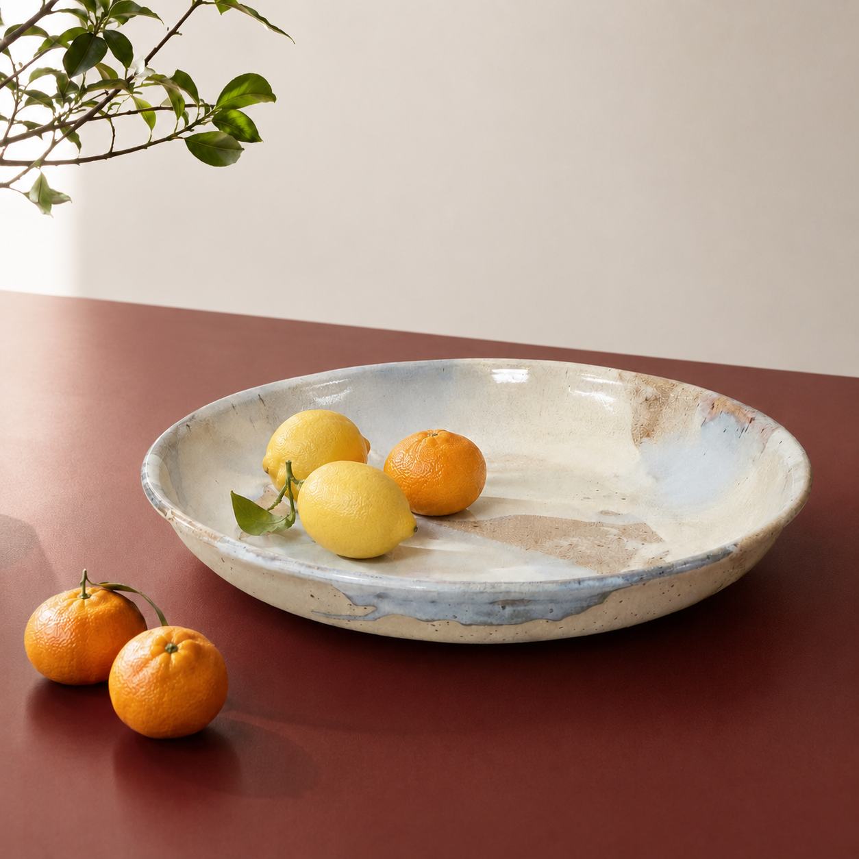 stort keramik fad i blå og grønne nuancer står på et rødt bord med citrusfrugter. 